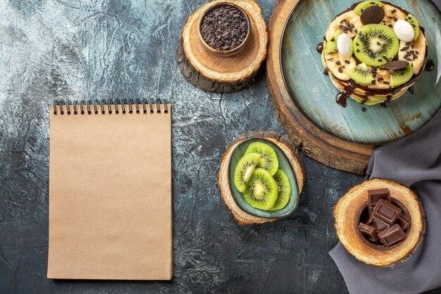 Vista de cima deliciosas panquecas com frutas fatiadas e chocolate na superfície cinza-escuro bolo cor doce café da manhã açúcar frutas sobremesa