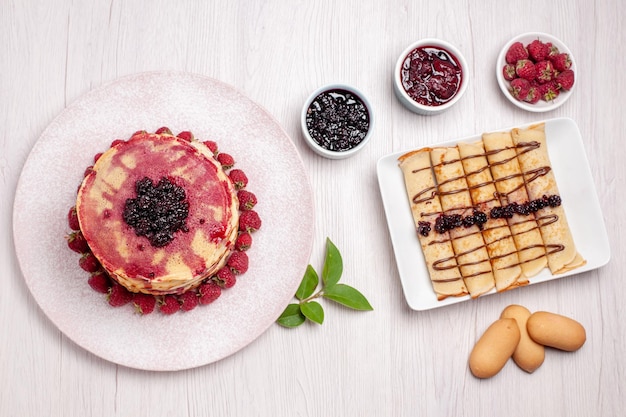 Vista de cima deliciosas panquecas com morangos e geléia na mesa branca, torta, biscoito doce, bolo de frutas, baga