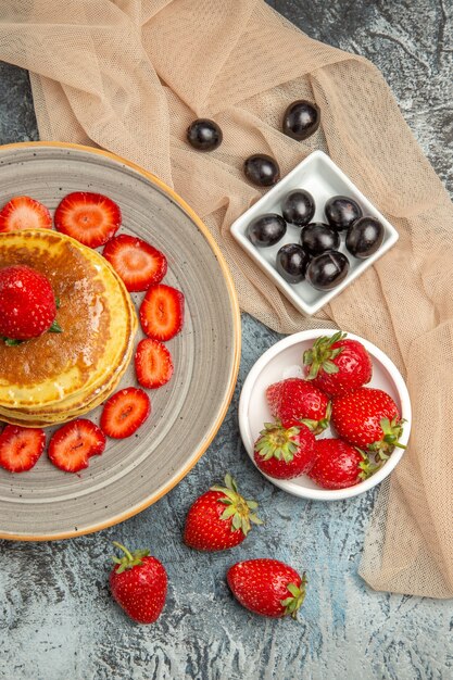 Vista de cima deliciosas panquecas com morangos frescos em uma superfície clara de bolo doce de frutas