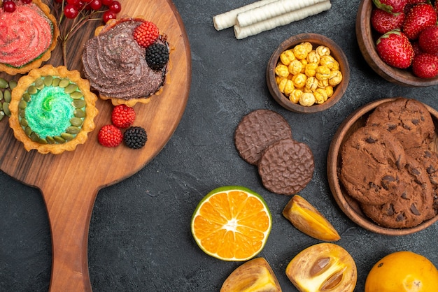 Vista de cima deliciosos bolinhos com biscoitos e frutas em uma mesa escura de torta doce