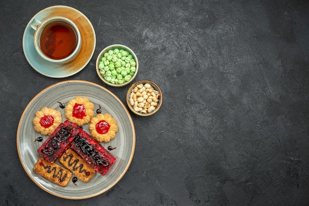 Vista de cima deliciosos bolos de frutas com biscoitos e uma xícara de chá no fundo escuro torta de biscoito de açúcar biscoito bolo de chá doce