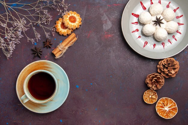 Vista de cima deliciosos doces de coco pequeno e redondo formado com uma xícara de chá no fundo escuro coco doce chá doce bolo cookies