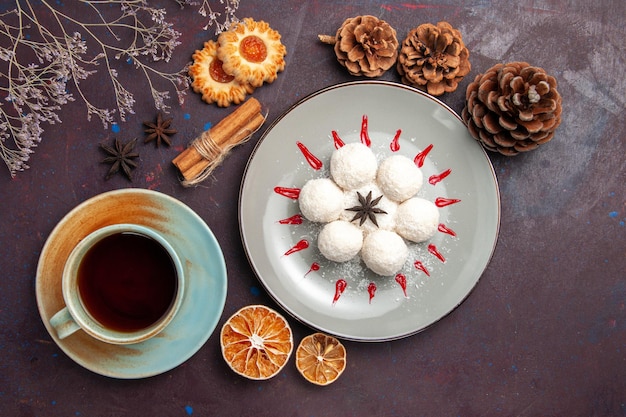 Vista de cima deliciosos doces de coco pequeno e redondo formado com uma xícara de chá no fundo escuro doce de coco chá doce bolo cookie