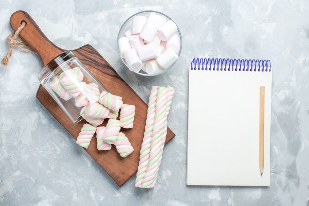 Vista de cima, deliciosos marshmallows coloridos formaram docinhos na mesa branca clara.
