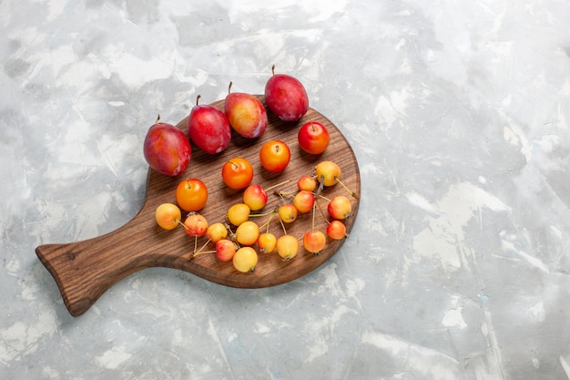 Vista de cima diferentes ameixas formadas frutas ácidas e frescas com cerejas na mesa branca clara.