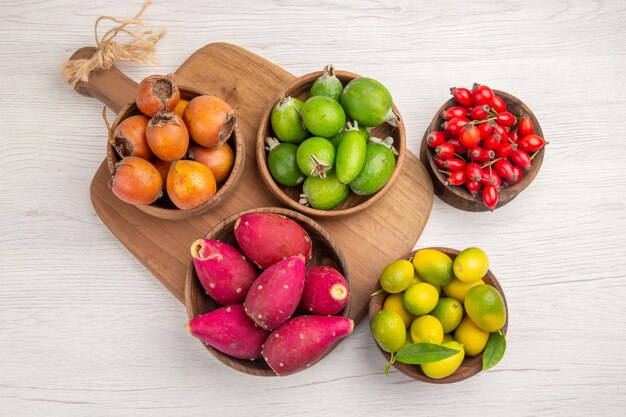 Vista de cima diferentes frutas feijoas bagas e outras frutas dentro de pratos em fundo branco alimentos maduros cor exótica