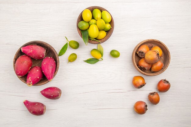 Vista de cima diferentes frutas frescas dentro de pratos em fundo branco frutas dieta madura tropical cor exótica vida saudável