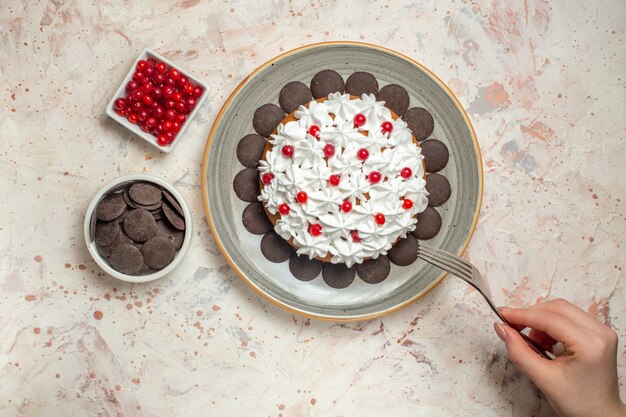 Vista de cima do bolo com creme de confeiteiro, frutas e chocolate no garfo de tigelas em mão feminina