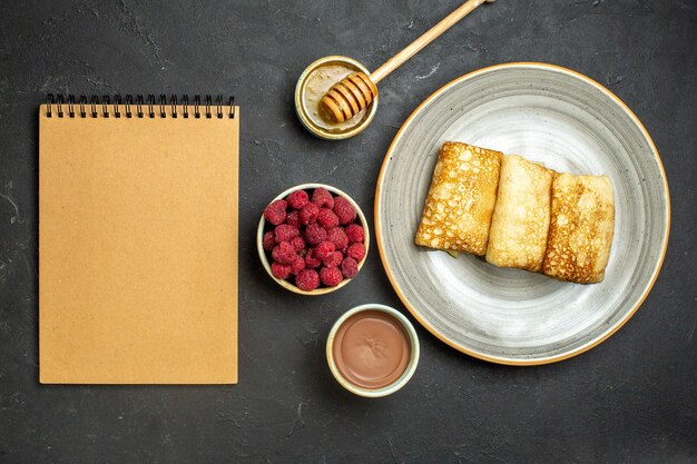 Vista de cima do fundo do jantar com deliciosas panquecas de mel e chocolate de framboesa ao lado do caderno em fundo preto