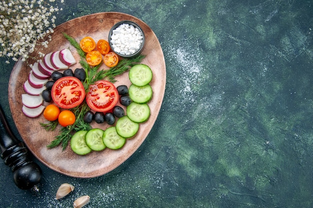 Vista de cima do sal de azeitonas de legumes frescos picados em um prato marrom e o martelo de cozinha no lado direito na mesa de cores verdes pretas