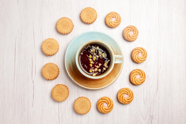 Vista de cima em close-up, chá com biscoitos, xícara branca de chá de ervas e biscoitos apetitosos ao redor sobre a mesa branca