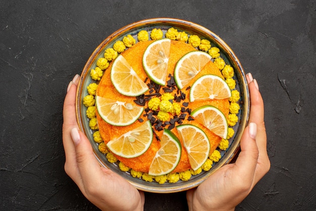 Foto grátis vista de cima em close-up frutas cítricas e bolo apetitoso de chocolate com frutas cítricas e chocolate nas mãos sobre a mesa preta