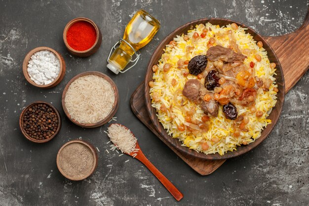 Vista de cima em close-up pilaf de especiarias na tábua de corte garrafa de especiarias colher de óleo tigela de arroz