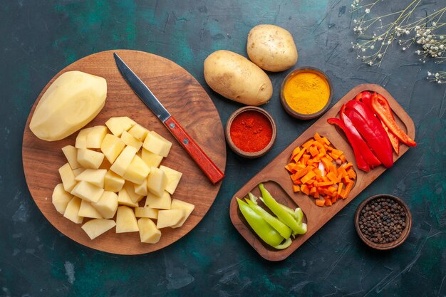 Vista de cima em fatias de batatas frescas com temperos e pimentões fatiados em uma mesa azul escura