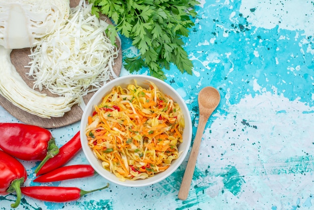 Vista de cima em fatias de legumes frescos longos e finos pedaços de salada dentro do prato com repolho verde no chão azul brilhante comida refeição salada de vegetais