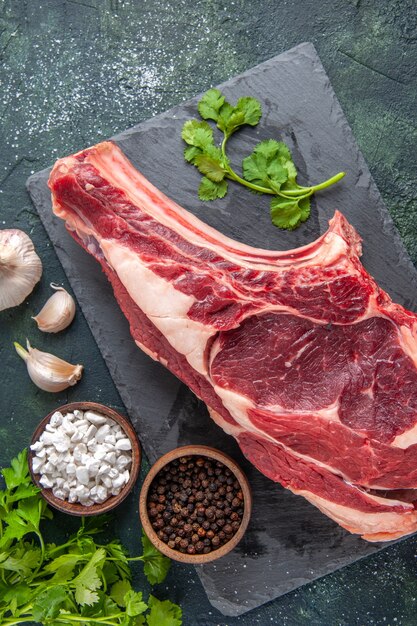 Vista de cima em uma fatia grande de carne crua com pimenta e verduras na superfície escura