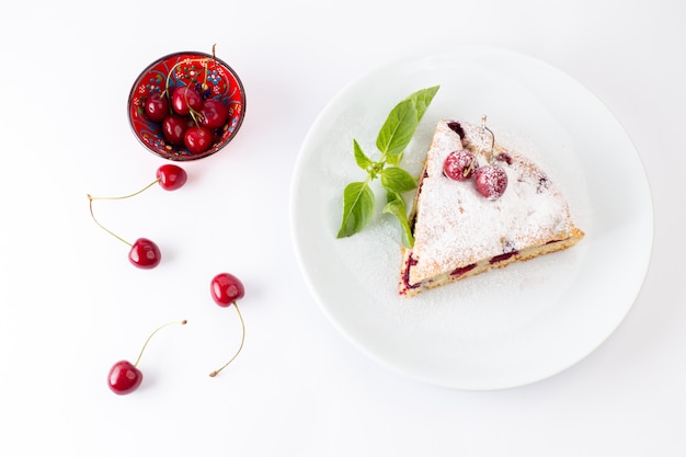 Vista de cima fatia de bolo de cereja delicioso e gostoso dentro de um prato branco junto com cerejas frescas no bolo de mesa branco doce assar