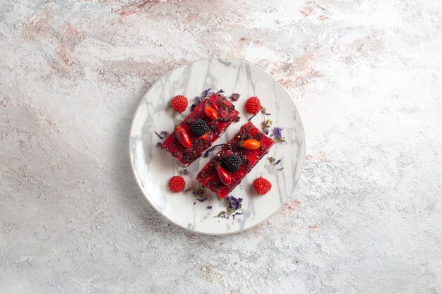 Vista de cima fatias de bolo de frutas saborosas com creme vermelho sobre fundo branco