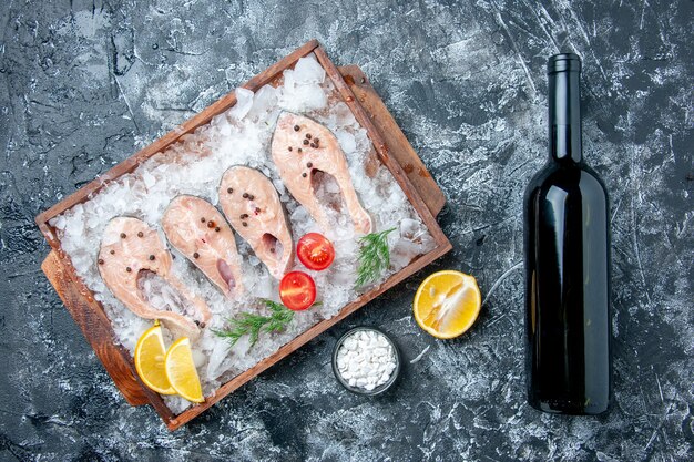 Vista de cima fatias de peixe cru com gelo na tábua de madeira sal marinho em uma pequena tigela com garrafa de vinho na mesa