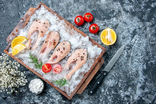 Vista de cima fatias de peixe cru com gelo na tábua de madeira sal marinho em uma pequena tigela de faca no espaço livre da mesa