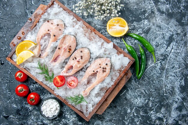 Vista de cima fatias de peixe cru com gelo na tábua de madeira sal marinho em uma tigela pequena de legumes na mesa
