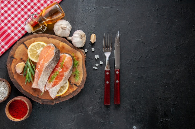 Vista de cima fatias de peixe fresco com fatias de limão, alho e temperos na mesa escura