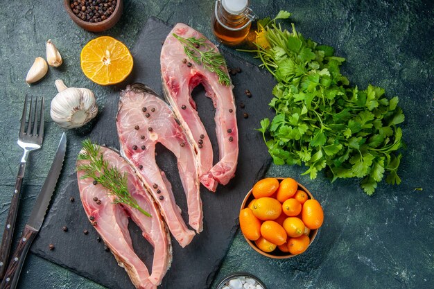 vista de cima fatias de peixe fresco com verduras e kumquats em fundo azul escuro