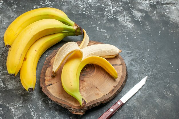 Vista de cima, fonte de nutrição, pacote de bananas frescas e descascadas em faca de tábua de madeira em fundo cinza