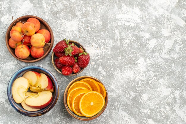 Vista de cima frutas fatiadas, maçãs e laranjas com bagas no fundo branco frutas frescas vitaminas maduras saúde