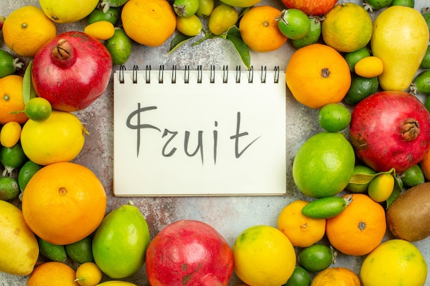 Foto grátis vista de cima frutas frescas diferentes frutas maduras com frutas escritas no bloco de notas no fundo branco saborosa cor da baga dieta saúde árvore madura