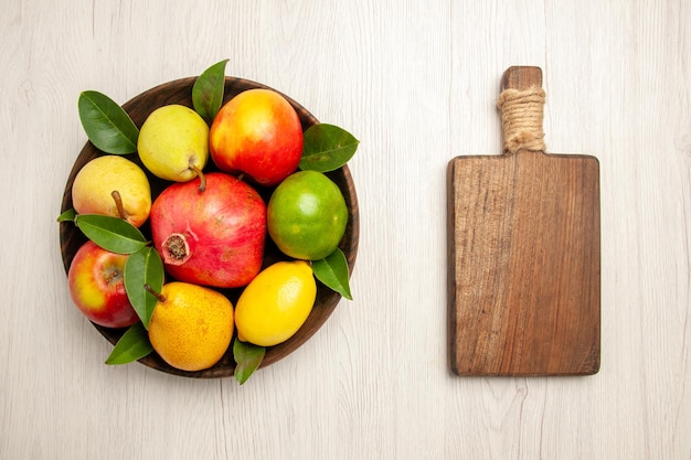 Vista de cima frutas frescas maçãs pêras e outras frutas dentro do prato na mesa branca frutas maduras árvore cor suave muitas frescas