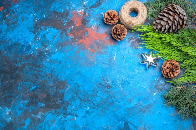 Vista de cima galhos de pinheiro com pinhas de palha de fio de palha pingente de estrela de natal em fundo azul-vermelho com espaço livre