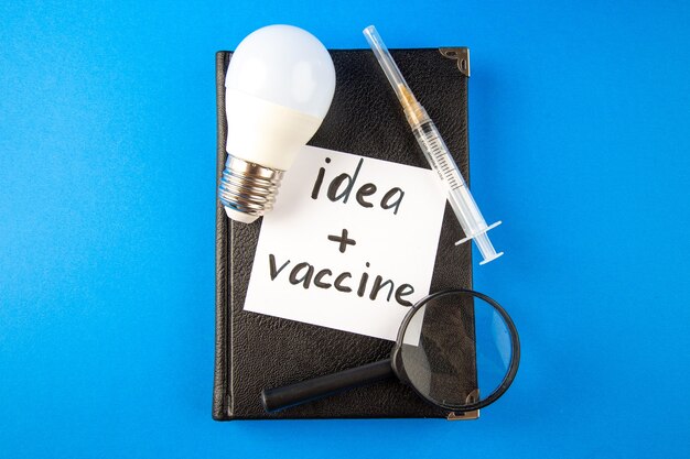 vista de cima injeção de antivírus com ampliador de caderno e lâmpada na superfície azul vírus laboratório medicina hospital drogas covidemia cura pandêmica saúde