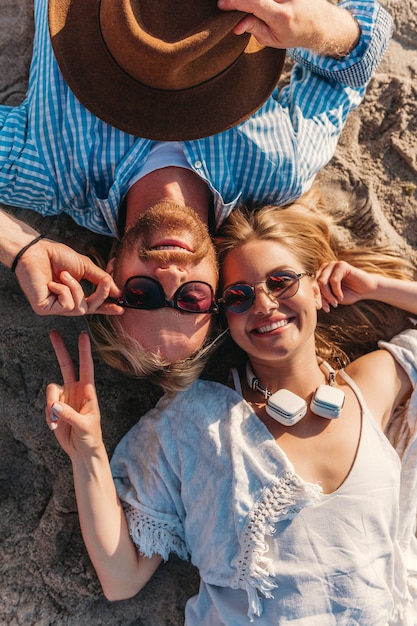 Vista de cima, jovem atraente, sorridente, feliz, homem e mulher com óculos de sol, deitado na praia de areia