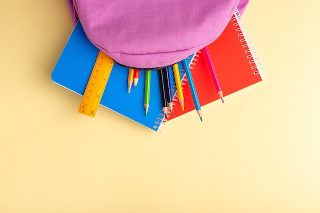 Foto grátis vista de cima lápis coloridos com cadernos e bolsa roxa na mesa amarelo claro bloco de notas de caneta escolar.