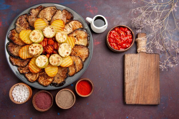 Vista de cima, legumes assados, batatas e berinjelas com temperos diferentes em uma mesa escura