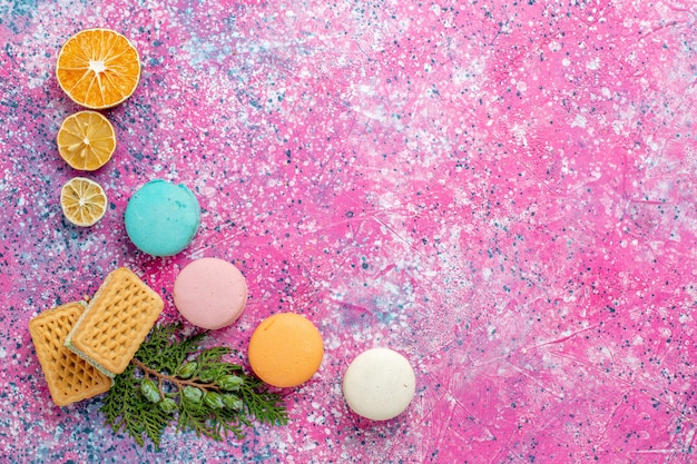 Foto grátis vista de cima macarons franceses coloridos com waffles no bolo de mesa rosa doce assar torta biscoito açúcar