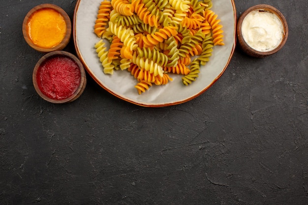 Vista de cima macarrão italiano cozido macarrão espiral incomum com temperos na mesa escura refeição de massa cozinhando prato jantar