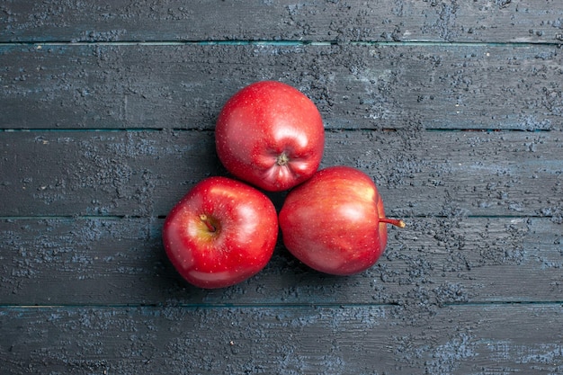 Vista de cima, maçãs vermelhas frescas, frutas maduras e maduras alinhadas na mesa azul escura, muitas frutas vermelhas, plantas de árvore de cor fresca