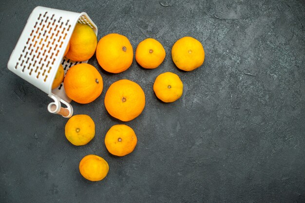 Vista de cima, mandarinas e laranjas espalhadas da cesta de plástico na superfície escura