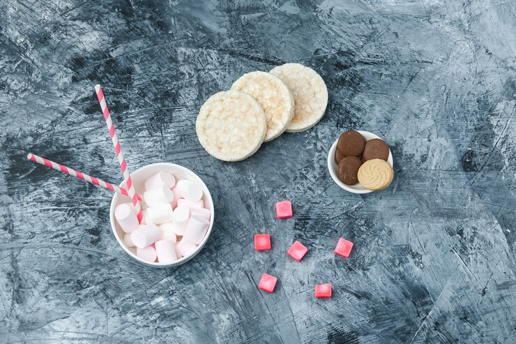 Foto grátis vista de cima, marshmallows e canas de açúcar na xícara com bolachas de arroz, biscoitos e doces na superfície de mármore azul escuro. horizontal