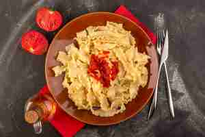 Foto grátis vista de cima massa italiana cozida com molho de tomate dentro do prato com talheres e tomates