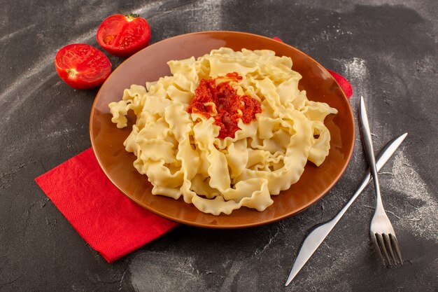 Vista de cima massa italiana cozida com talheres de molho de tomate e tomates dentro do prato