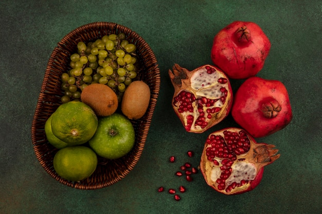 Vista de cima metades de romã com tangerinas, uvas de maçã e kiwi em uma cesta