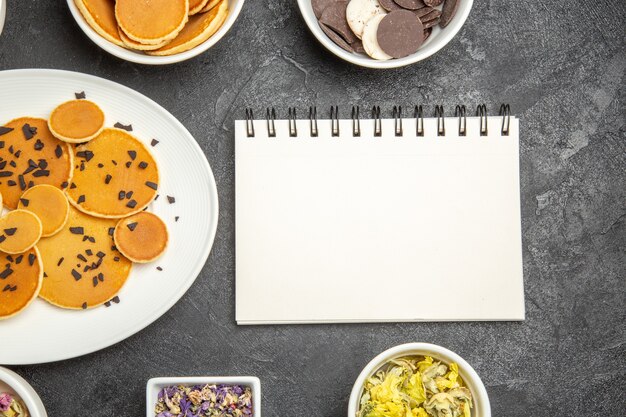 Vista de cima panquecas deliciosas com chá e biscoitos na mesa escura