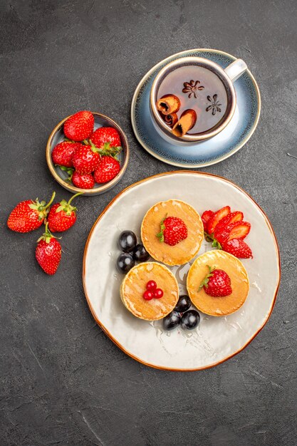 Vista de cima panquecas gostosas com frutas e uma xícara de chá na superfície cinza bolo de frutas