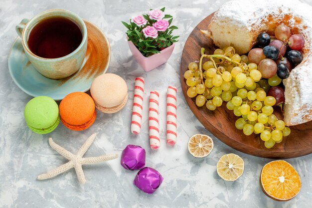 Vista de cima para baixo bolo de confeiteiro com chá de uvas frescas e macarons franceses em uma mesa branca.