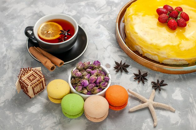 Vista de cima para baixo, delicioso bolo de frutas com calda amarela de macarons franceses e xícara de chá na mesa branca