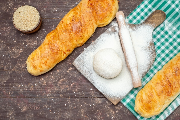 Foto grátis vista de cima pastelaria saborosa fresca pão longo formado pastelaria no tecido quadriculado com farinha na mesa de madeira marrom pão massa folhada pão comida refeição