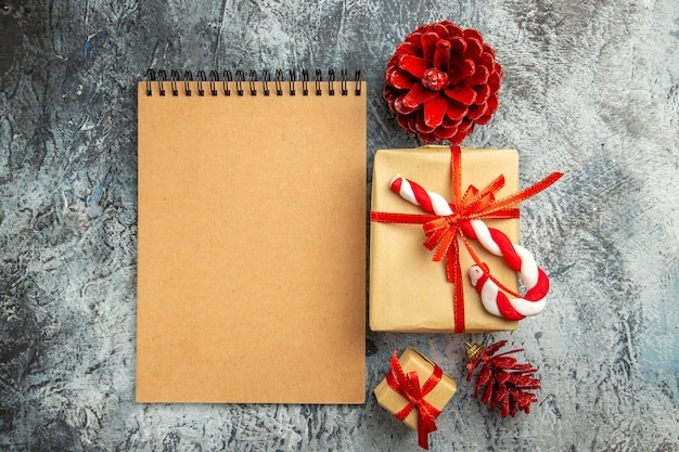 Vista de cima pequeno presente amarrado com pinhas de caderno de doces de Natal de fita vermelha em fundo cinza